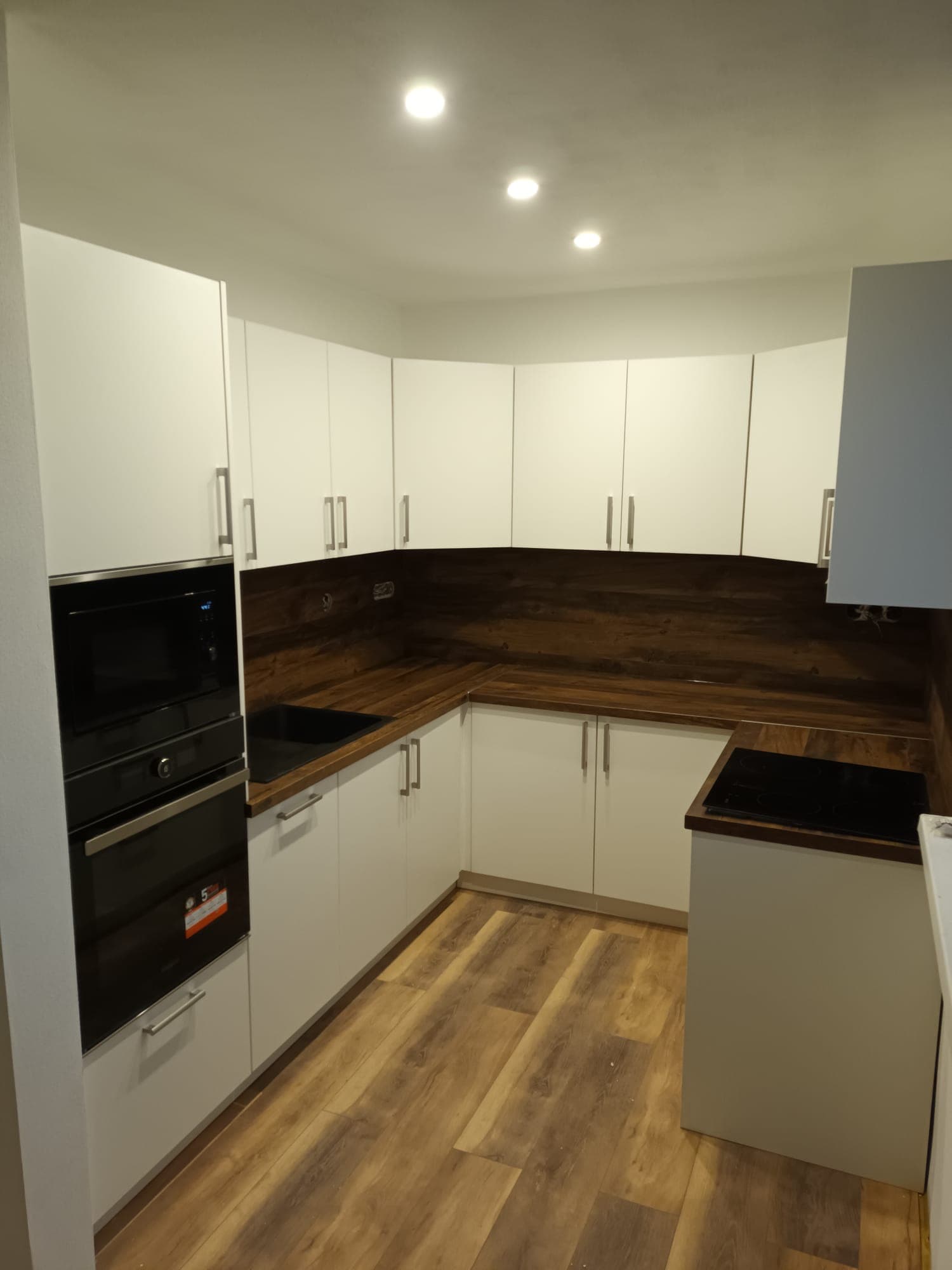 Biela rohová kuchyňa s drevenými prvkami